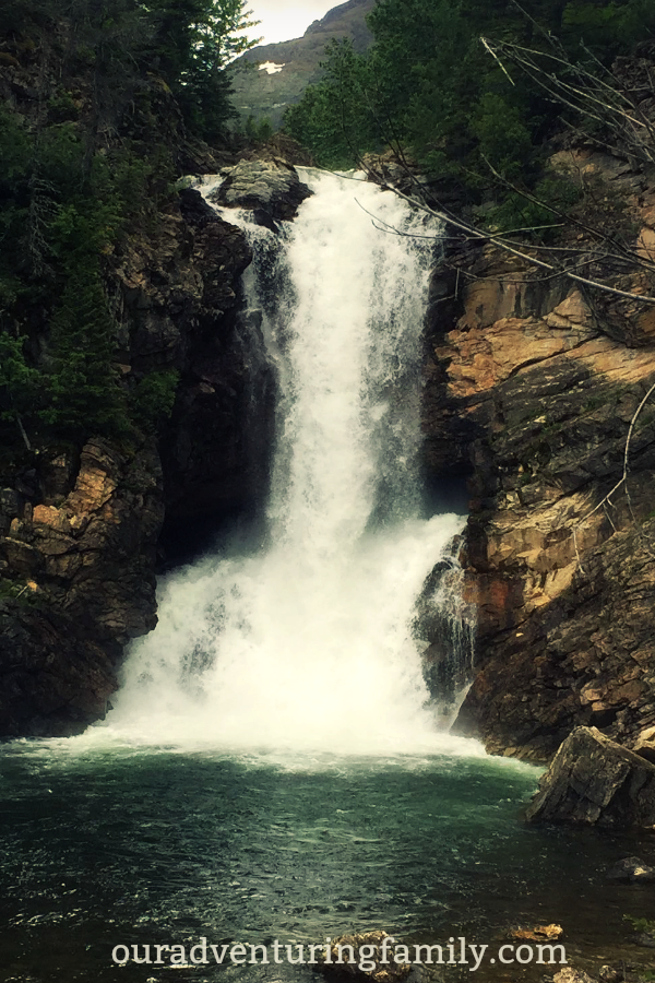 The first part of the trail to Running Eagle falls at Glacier National Park is fairly flat and level. Once you get to the river though, the trail is rocky and you have to cross a narrow log bridge to get to the best viewing spot. Still, it's a short hike from the trailhead and SO pretty! More at ouradventuringfamily.com. #shortglacierhikes #worththehike